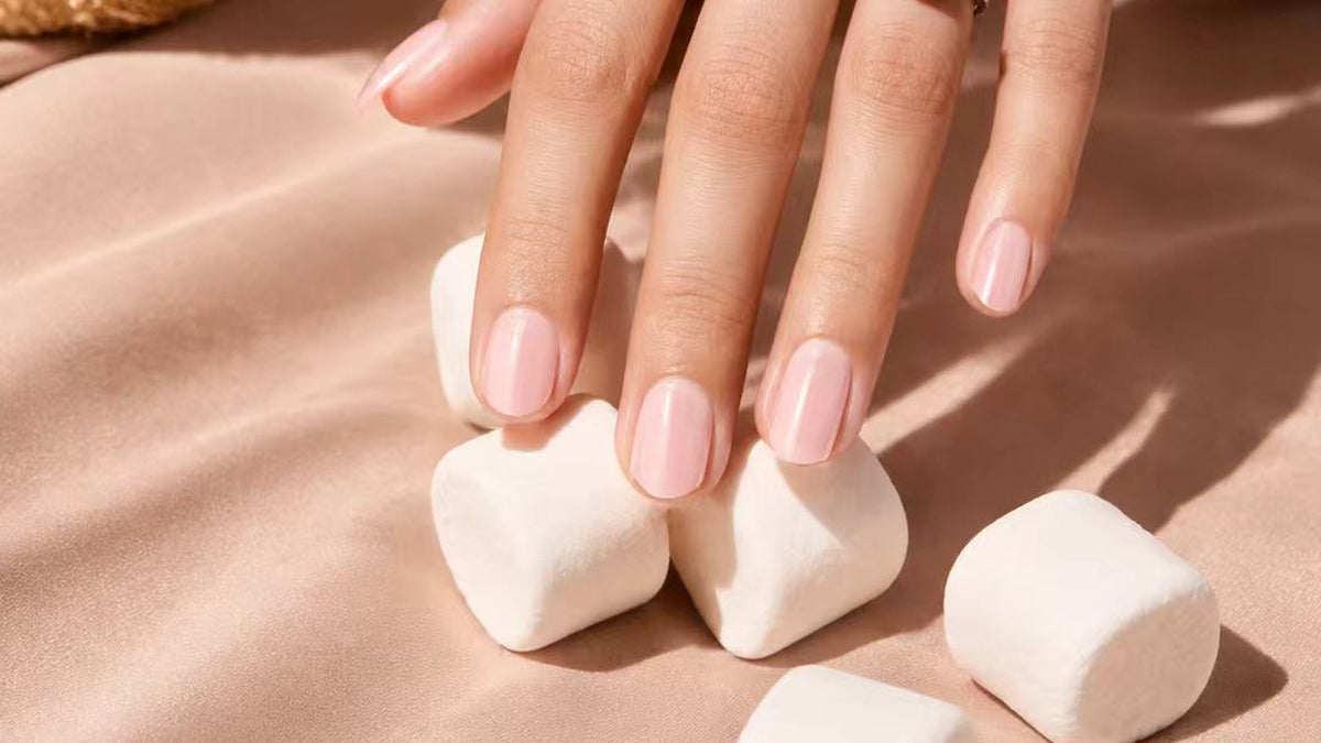Hand mit zartrosa Press-on Nails von L'Adele auf Satin, neben Marshmallows